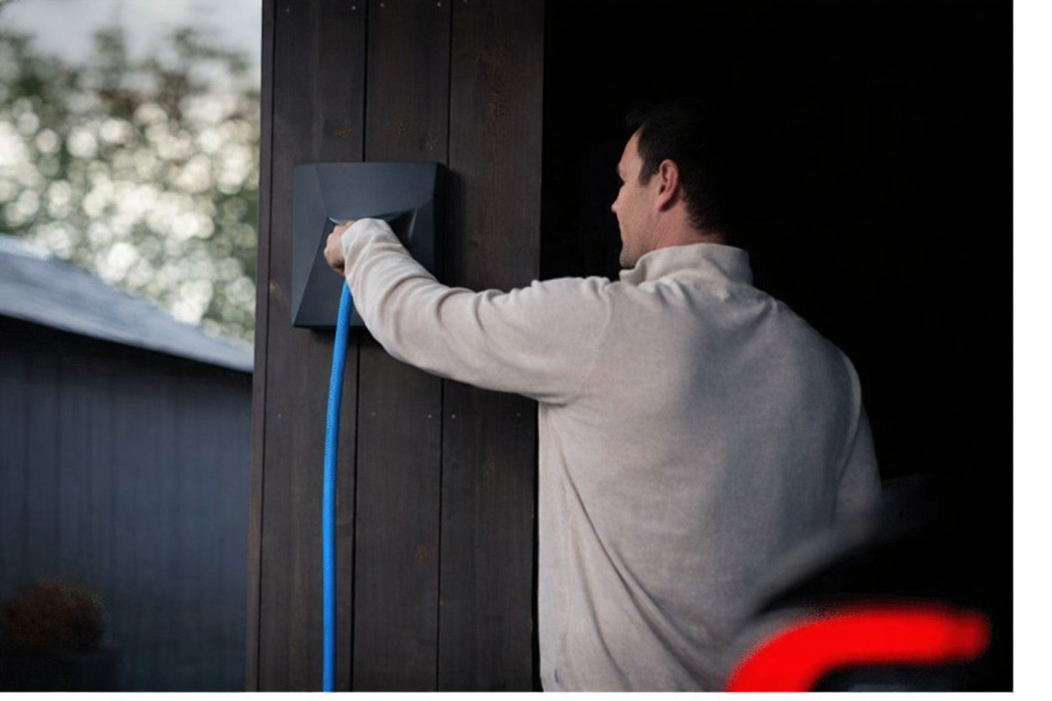 Man ansluter blå laddkabel till svart Zaptec laddbox på träpanel.