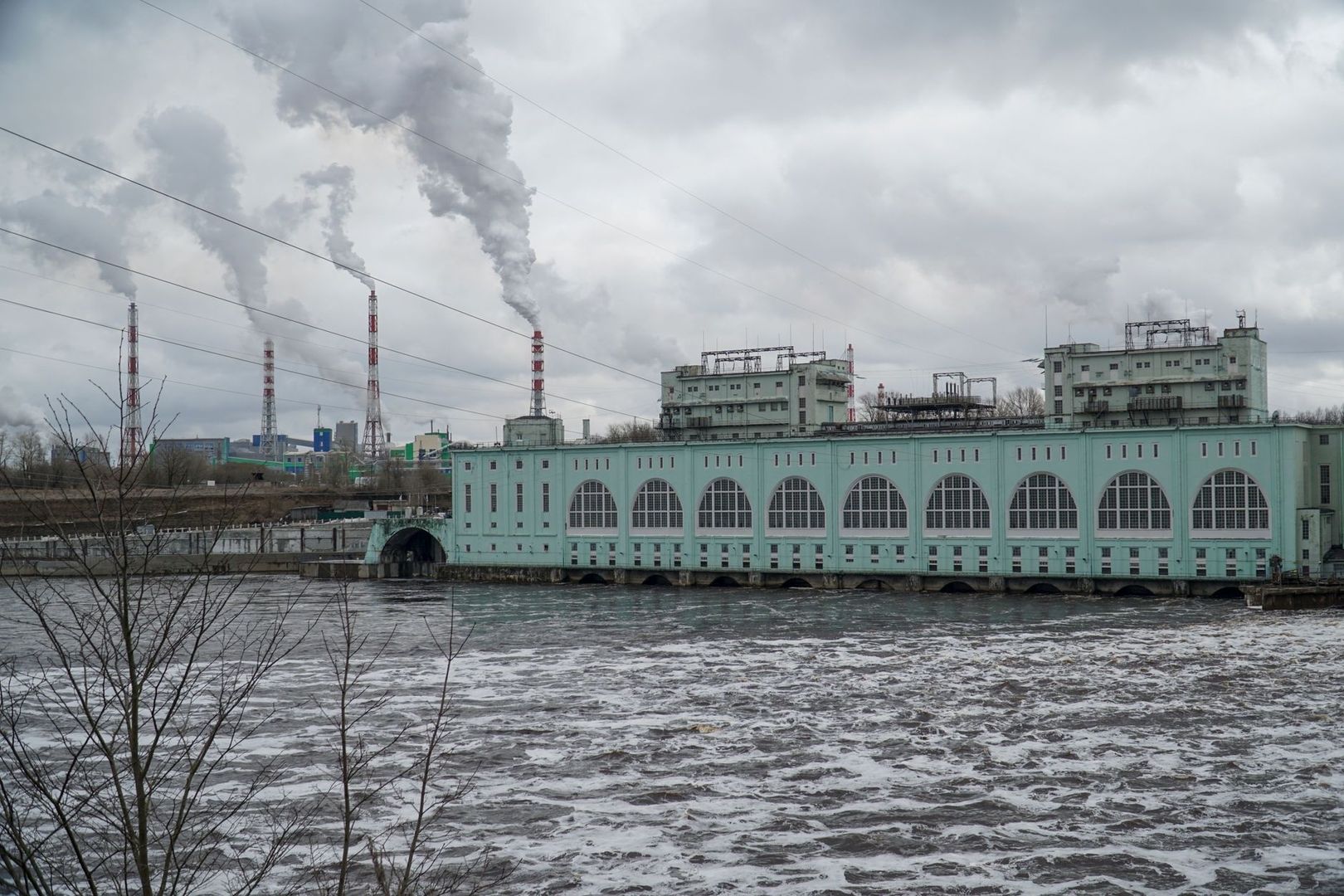 Industribyggnad vid ström med skorstenar och rök under molnig himmel