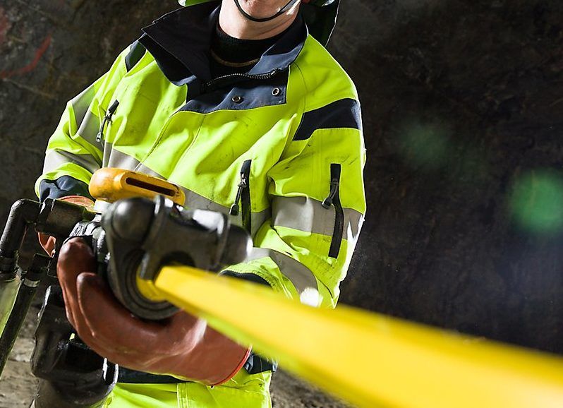 En person i skyddskläder arbetar med en bergspräckare i en gruvliknande miljö.